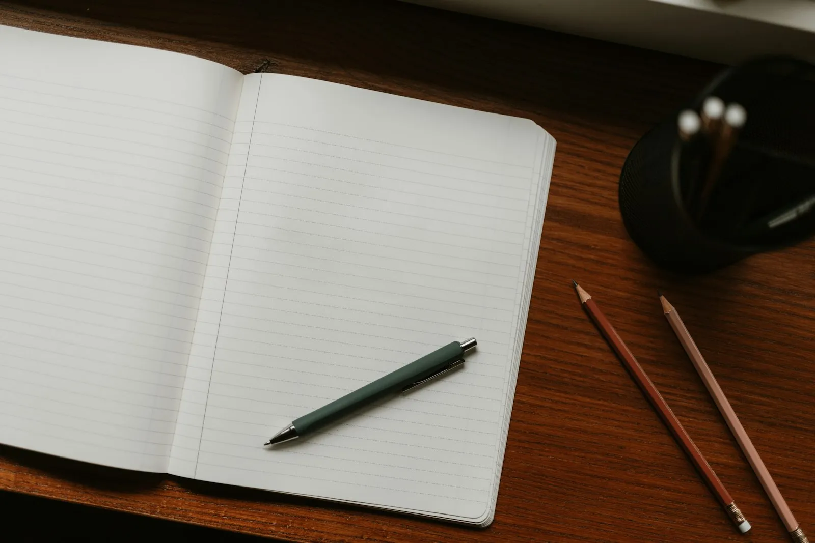 An open notebook with a pen and pencils on a wooden desk